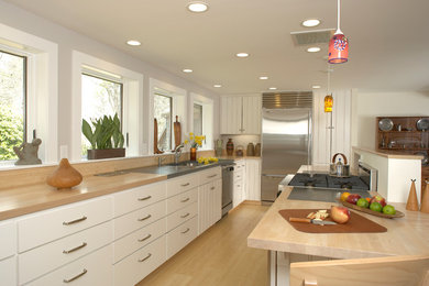 Modelo de cocina actual con puertas de armario blancas, encimera de madera y electrodomésticos de acero inoxidable