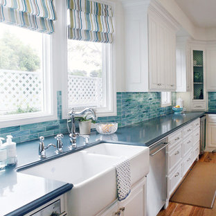 Mid-sized traditional single-wall open plan kitchen in Los Angeles with a farmhouse sink, raised-panel cabinets, white cabinets, stainless steel appliances, blue splashback, quartz benchtops, glass tile splashback, medium hardwood floors, with island and blue benchtop.