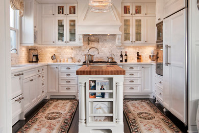 Exempel på ett klassiskt u-kök, med en undermonterad diskho, vita skåp, beige stänkskydd, integrerade vitvaror, en köksö, stänkskydd i travertin och luckor med infälld panel