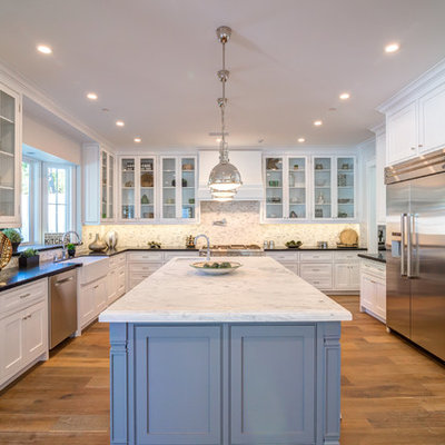 Example of a large transitional u-shaped medium tone wood floor eat-in kitchen design in Los Angeles with a farmhouse sink, glass-front cabinets, white cabinets, solid surface countertops, multicolored backsplash, porcelain backsplash, stainless steel appliances and an island