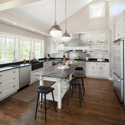 Example of a transitional u-shaped kitchen design in Portland Maine with a farmhouse sink, recessed-panel cabinets, white cabinets, white backsplash, subway tile backsplash and stainless steel appliances