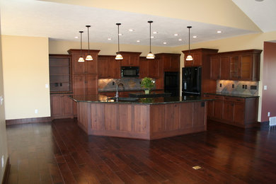 Example of a mid-sized arts and crafts l-shaped dark wood floor and brown floor open concept kitchen design in Omaha with an undermount sink, shaker cabinets, dark wood cabinets, granite countertops, black appliances, an island, beige backsplash and ceramic backsplash