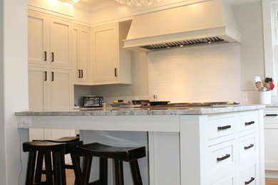 Photo of a large classic u-shaped enclosed kitchen in Seattle with a submerged sink, raised-panel cabinets, white cabinets, granite worktops, white splashback, ceramic splashback, stainless steel appliances, medium hardwood flooring and an island.