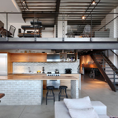 Small urban galley concrete floor and gray floor open concept kitchen photo in Seattle with an island, flat-panel cabinets, light wood cabinets, wood countertops, gray backsplash, brick backsplash, stainless steel appliances and an undermount sink