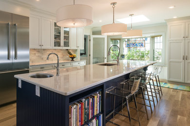 Example of a mid-sized transitional l-shaped medium tone wood floor and brown floor open concept kitchen design in Boston with an undermount sink, shaker cabinets, white cabinets, quartz countertops, gray backsplash, subway tile backsplash, stainless steel appliances and an island