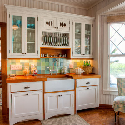 Eat-in kitchen - mid-sized tropical galley dark wood floor and brown floor eat-in kitchen idea in Miami with wood countertops, a farmhouse sink, green backsplash, shaker cabinets, white cabinets, glass tile backsplash and no island