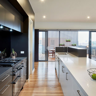 Contemporary galley kitchen in Melbourne with an undermount sink, flat-panel cabinets, black cabinets, black splashback, black appliances, light hardwood floors, with island and beige floor.