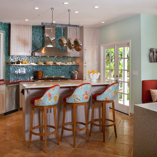 Esempio di una cucina tropicale di medie dimensioni con lavello sottopiano, ante con riquadro incassato, ante bianche, paraspruzzi blu, paraspruzzi con piastrelle a mosaico, elettrodomestici in acciaio inossidabile, isola e top in vetro riciclato