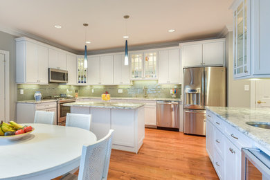 Photo of a large classic u-shaped kitchen/diner in DC Metro with a submerged sink, shaker cabinets, white cabinets, granite worktops, grey splashback, glass tiled splashback, stainless steel appliances, an island, medium hardwood flooring and brown floors.