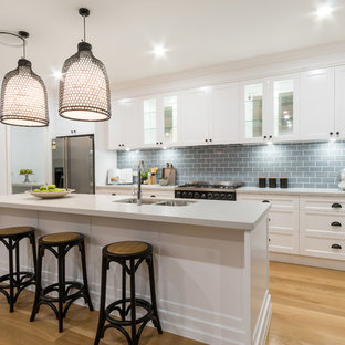 Inspiration for a beach style galley kitchen in Townsville with a double-bowl sink, shaker cabinets, white cabinets, grey splashback, subway tile splashback, stainless steel appliances, light hardwood floors and with island.