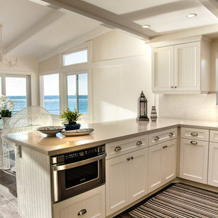 Photo of a mid-sized beach style l-shaped open plan kitchen in San Diego with an undermount sink, white cabinets, quartzite benchtops, white splashback, stainless steel appliances, louvered cabinets, stone slab splashback, medium hardwood floors, a peninsula and grey floor.