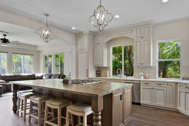 Inspiration for a traditional l-shaped open plan kitchen in San Diego with recessed-panel cabinets, beige cabinets, beige splashback, stainless steel appliances, dark hardwood flooring, an island, brown floors and white worktops.
