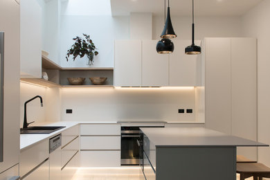 This is an example of a medium sized contemporary l-shaped kitchen in Melbourne with white splashback, porcelain splashback, black appliances, an island and grey worktops.