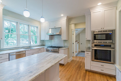 Example of a large classic u-shaped medium tone wood floor and brown floor enclosed kitchen design in Boston with an undermount sink, stainless steel appliances, shaker cabinets, white cabinets, marble countertops, white backsplash, subway tile backsplash and an island