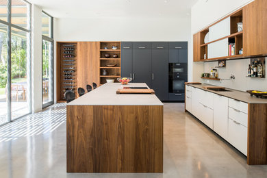 Inspiration for a contemporary galley concrete floor and gray floor eat-in kitchen remodel in Houston with flat-panel cabinets, white cabinets, black appliances, an island, a single-bowl sink, quartz countertops, white backsplash and glass sheet backsplash