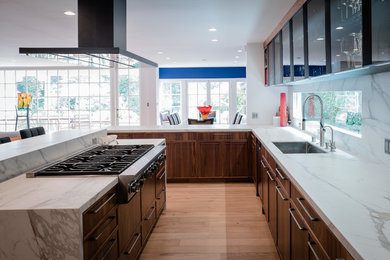 This is an example of an expansive modern l-shaped kitchen/diner in Los Angeles with a submerged sink, flat-panel cabinets, medium wood cabinets, engineered stone countertops, white splashback, marble splashback, black appliances, medium hardwood flooring, an island, beige floors and white worktops.