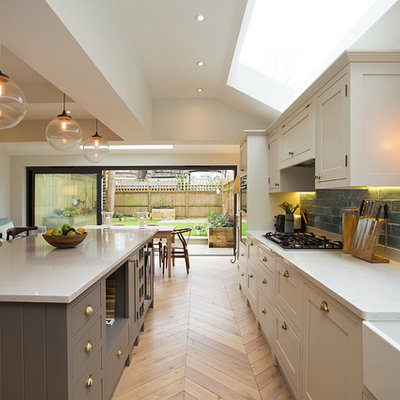 Open concept kitchen - mid-sized transitional light wood floor and beige floor open concept kitchen idea in London with a farmhouse sink, shaker cabinets, blue backsplash, subway tile backsplash, an island, beige cabinets and beige countertops