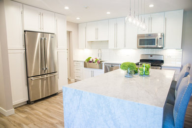 Mid-sized transitional u-shaped light wood floor and brown floor eat-in kitchen photo in Chicago with a farmhouse sink, shaker cabinets, white cabinets, marble countertops, white backsplash, subway tile backsplash, stainless steel appliances and an island