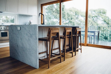 Inspiration for a contemporary l-shaped open plan kitchen in Sydney with white cabinets, marble worktops, grey splashback, stone slab splashback, stainless steel appliances, medium hardwood flooring, an island, a submerged sink and recessed-panel cabinets.