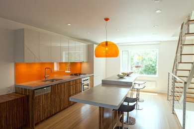 На фото: кухня в современном стиле с плоскими фасадами, оранжевым фартуком, столешницей из бетона и фартуком из стекла