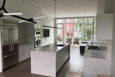 Medium sized modern u-shaped kitchen/diner in New York with a submerged sink, flat-panel cabinets, white cabinets, engineered stone countertops, stainless steel appliances, laminate floors, an island and brown floors.