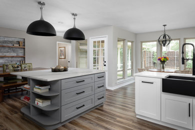 Inspiration for a large contemporary l-shaped medium tone wood floor and brown floor kitchen remodel in Dallas with a farmhouse sink, shaker cabinets, white cabinets, quartzite countertops, gray backsplash, glass tile backsplash, black appliances, an island and white countertops
