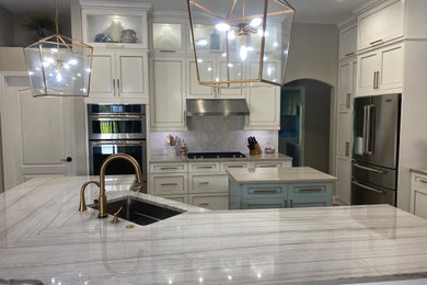 Example of a mid-sized transitional l-shaped vinyl floor and brown floor eat-in kitchen design in Tampa with an undermount sink, shaker cabinets, white cabinets, quartzite countertops, white backsplash, stone tile backsplash, stainless steel appliances, two islands and white countertops