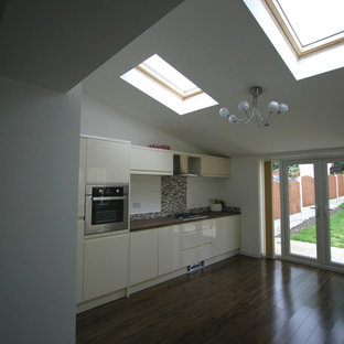 Design ideas for a mid-sized contemporary single-wall open plan kitchen in Other with a double-bowl sink, flat-panel cabinets, white cabinets, laminate benchtops, multi-coloured splashback, ceramic splashback, stainless steel appliances, vinyl floors, no island, brown floor and pink benchtop.