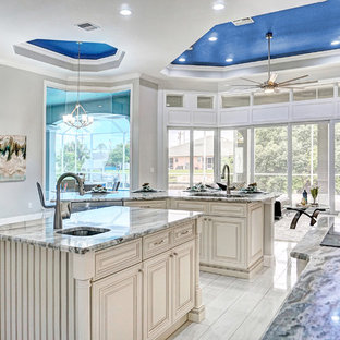 Photo of a mediterranean kitchen in Miami with an undermount sink, raised-panel cabinets, beige cabinets, stainless steel appliances, multiple islands, multi-coloured benchtop and white floor.