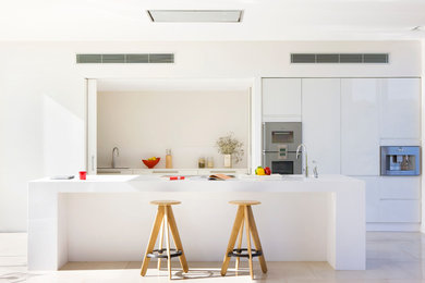 Mid-sized trendy galley travertine floor eat-in kitchen photo in Other with an integrated sink, flat-panel cabinets, white cabinets, solid surface countertops, white backsplash, stainless steel appliances and an island