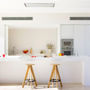 Mid-sized contemporary galley eat-in kitchen in Other with an integrated sink, flat-panel cabinets, white cabinets, solid surface benchtops, white splashback, stainless steel appliances, travertine floors and with island.