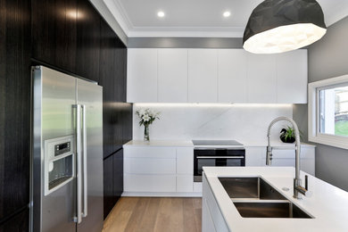 Inspiration for a medium sized contemporary l-shaped open plan kitchen in Christchurch with a submerged sink, flat-panel cabinets, white cabinets, engineered stone countertops, multi-coloured splashback, porcelain splashback, stainless steel appliances, medium hardwood flooring, an island, brown floors and white worktops.