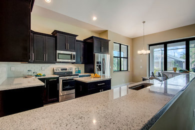 Eat-in kitchen - large transitional u-shaped eat-in kitchen idea in Miami with an undermount sink, recessed-panel cabinets, black cabinets, terrazzo countertops, white backsplash, ceramic backsplash, stainless steel appliances and an island