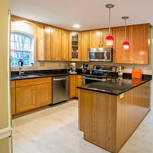 Design ideas for a traditional u-shaped eat-in kitchen in Baltimore with a double-bowl sink, shaker cabinets, medium wood cabinets, granite benchtops, stainless steel appliances, vinyl floors, a peninsula, grey floor and black benchtop.