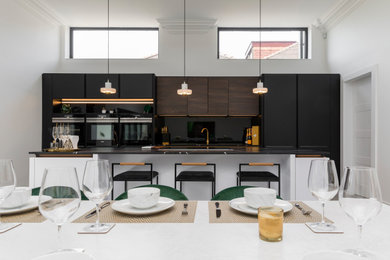 Inspiration for a large contemporary open plan kitchen in Glasgow with flat-panel cabinets, white cabinets, engineered stone countertops, black splashback, glass sheet splashback, black appliances, an island and black worktops.