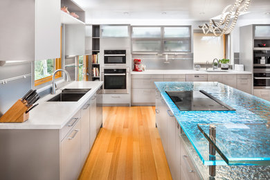 Inspiration for a large contemporary u-shaped light wood floor eat-in kitchen remodel in Los Angeles with flat-panel cabinets, beige cabinets, glass countertops, metallic backsplash, stainless steel appliances and two islands