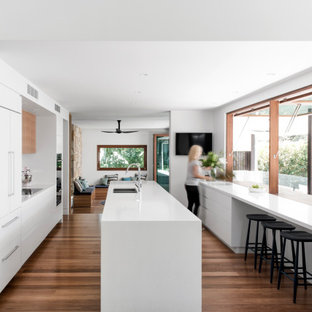 Design ideas for a contemporary galley kitchen in Sunshine Coast with an undermount sink, flat-panel cabinets, white cabinets, panelled appliances, medium hardwood floors, with island, brown floor and white benchtop.