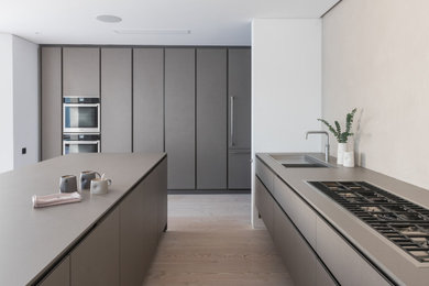 Photo of a large modern grey and white u-shaped kitchen in London with a submerged sink, flat-panel cabinets, grey cabinets, integrated appliances, an island, beige floors and grey worktops.