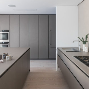 Photo of a large modern grey and white u-shaped kitchen in London with a submerged sink, flat-panel cabinets, grey cabinets, integrated appliances, an island, beige floors and grey worktops.