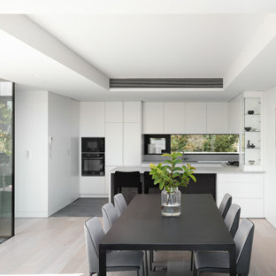 This is an example of a mid-sized modern u-shaped eat-in kitchen in Sydney with flat-panel cabinets, white cabinets, quartz benchtops, grey splashback, engineered quartz splashback, black appliances, ceramic floors, grey floor, grey benchtop, a peninsula and recessed.