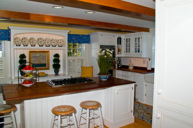 Modelo de cocina campestre con fregadero sobremueble, armarios con rebordes decorativos, puertas de armario blancas, encimera de madera y una isla