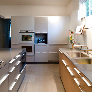 Inspiration pour une grand cuisine américaine minimaliste en U avec un évier 2 bacs, un placard à porte plane, une façade en inox, une crédence blanche, une crédence en feuille de verre, un plan de travail en verre, un électroménager en acier inoxydable, béton au sol et un îlot central.