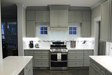 Photo of a contemporary kitchen/diner in Raleigh with a belfast sink, recessed-panel cabinets, grey cabinets, quartz worktops, white splashback, terracotta splashback, stainless steel appliances, dark hardwood flooring and an island.