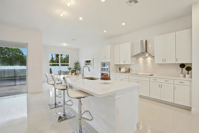 Example of a large minimalist l-shaped porcelain tile and beige floor open concept kitchen design in Miami with an undermount sink, shaker cabinets, white cabinets, quartz countertops, white backsplash, subway tile backsplash, stainless steel appliances and an island