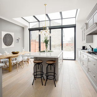 Inspiration for a large classic kitchen/diner in London with beaded cabinets, grey cabinets, white splashback, marble splashback, light hardwood flooring, an island, white worktops, marble worktops, a belfast sink and beige floors.