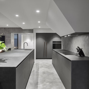 Large modern l-shaped open plan kitchen in Perth with concrete benchtops, grey splashback, stone slab splashback, concrete floors, with island, grey floor, grey benchtop, an undermount sink, flat-panel cabinets, grey cabinets and panelled appliances.