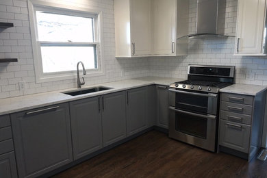 Example of a mid-sized classic l-shaped dark wood floor and brown floor eat-in kitchen design in Omaha with an undermount sink, raised-panel cabinets, gray cabinets, quartz countertops, white backsplash, subway tile backsplash, stainless steel appliances, no island and white countertops