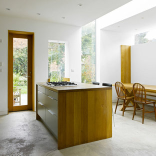 Medium sized contemporary kitchen/diner in London with flat-panel cabinets, concrete flooring, an island, grey floors, brown worktops, white cabinets and wood worktops.