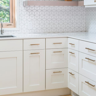 Immagine di una cucina ad U scandinava di medie dimensioni con lavello a doppia vasca, ante lisce, ante bianche, paraspruzzi bianco, paraspruzzi con piastrelle in ceramica, elettrodomestici in acciaio inossidabile, parquet chiaro, nessuna isola, pavimento giallo e top bianco