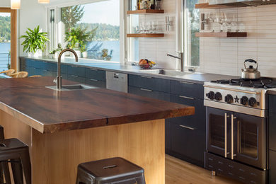 シアトルにある中くらいなミッドセンチュリースタイルのおしゃれなアイランドキッチン (アンダーカウンターシンク、フラットパネル扉のキャビネット、木材カウンター、シルバーの調理設備、無垢フローリング、黒いキャビネット) の写真